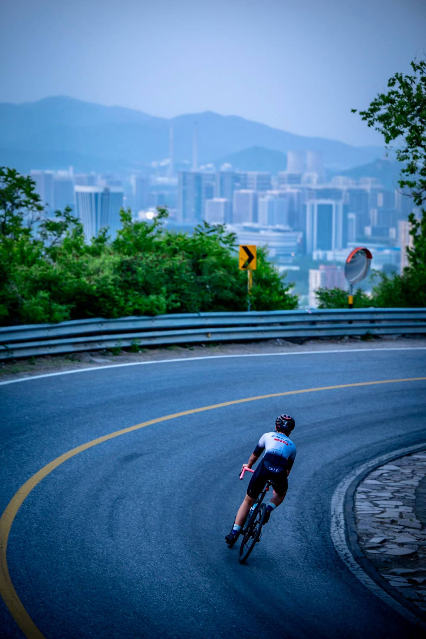 A cyclist descending a mountain road toward the city, seen from behind
