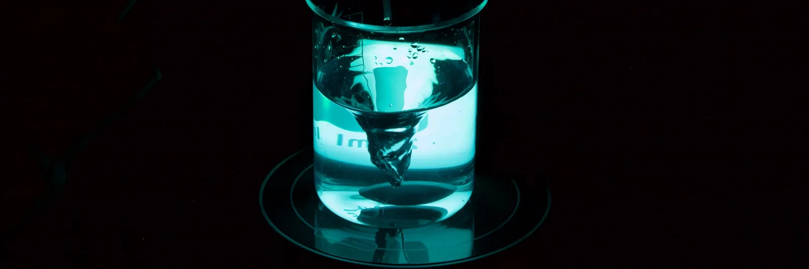 Stirred beaker vortex glowing teal in a darkened lab